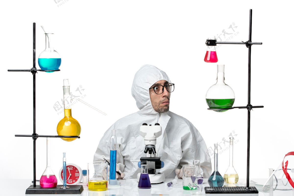 烧杯正面图穿着特殊防护服的男科学家拿着钢笔坐着医学玻璃科学
