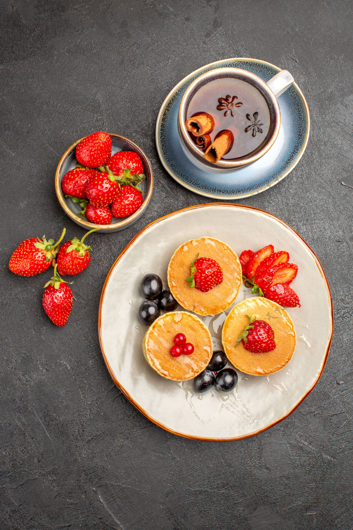 草莓顶视图小美味煎饼与水果和茶杯上的灰色表面馅饼蛋糕水果桌子杯子晚餐