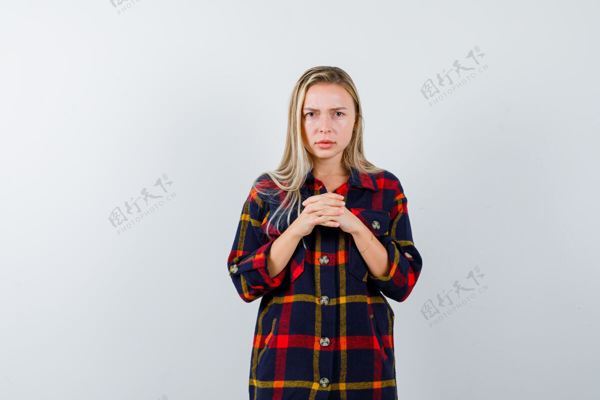 人照片中的年轻女士身穿格子衬衫 双手紧握在胸前 正面充满希望女孩肖像前面