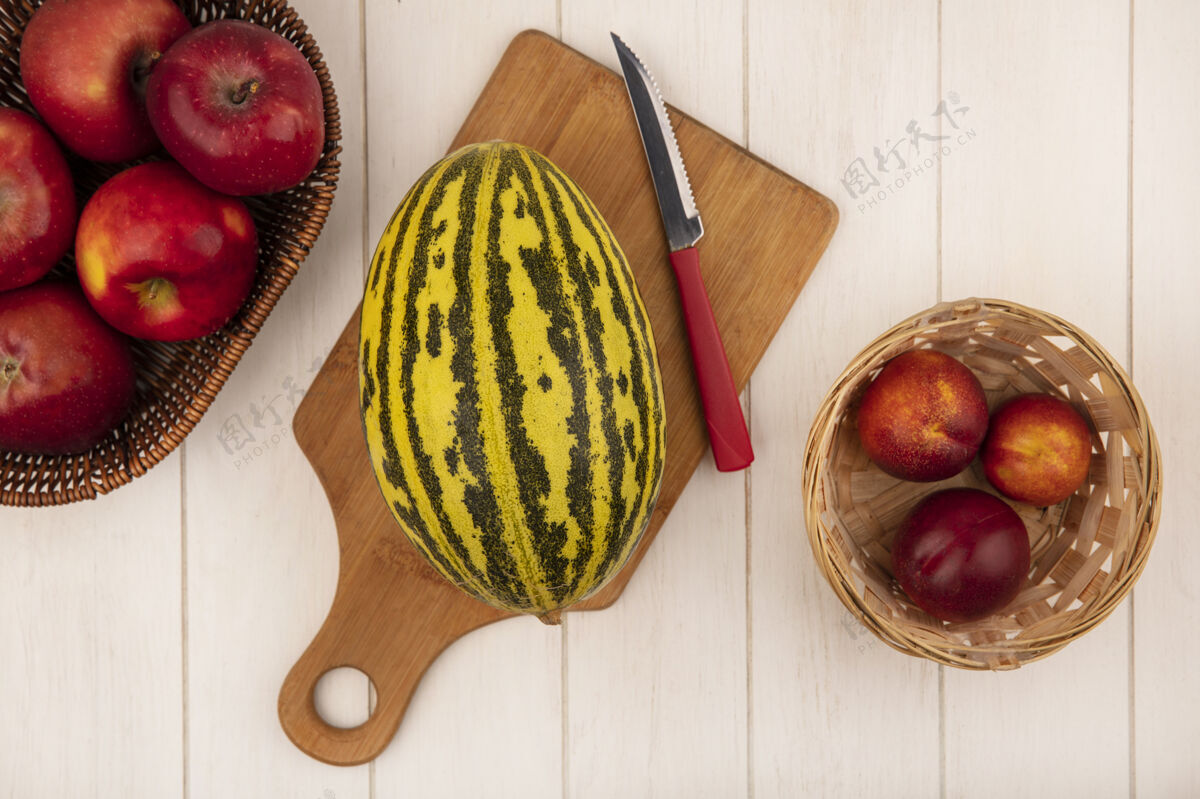 厨房新鲜的哈密瓜在一个木制的菜板上的俯视图 刀上放着苹果 桶上放着桃子 白色的木墙上刀苹果夏天