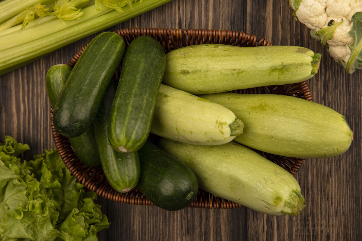 顶部顶视图新鲜的绿色蔬菜 如西葫芦和黄瓜在一个木桶与莴苣芹菜和花椰菜隔离在一个木墙上木材芹菜食品