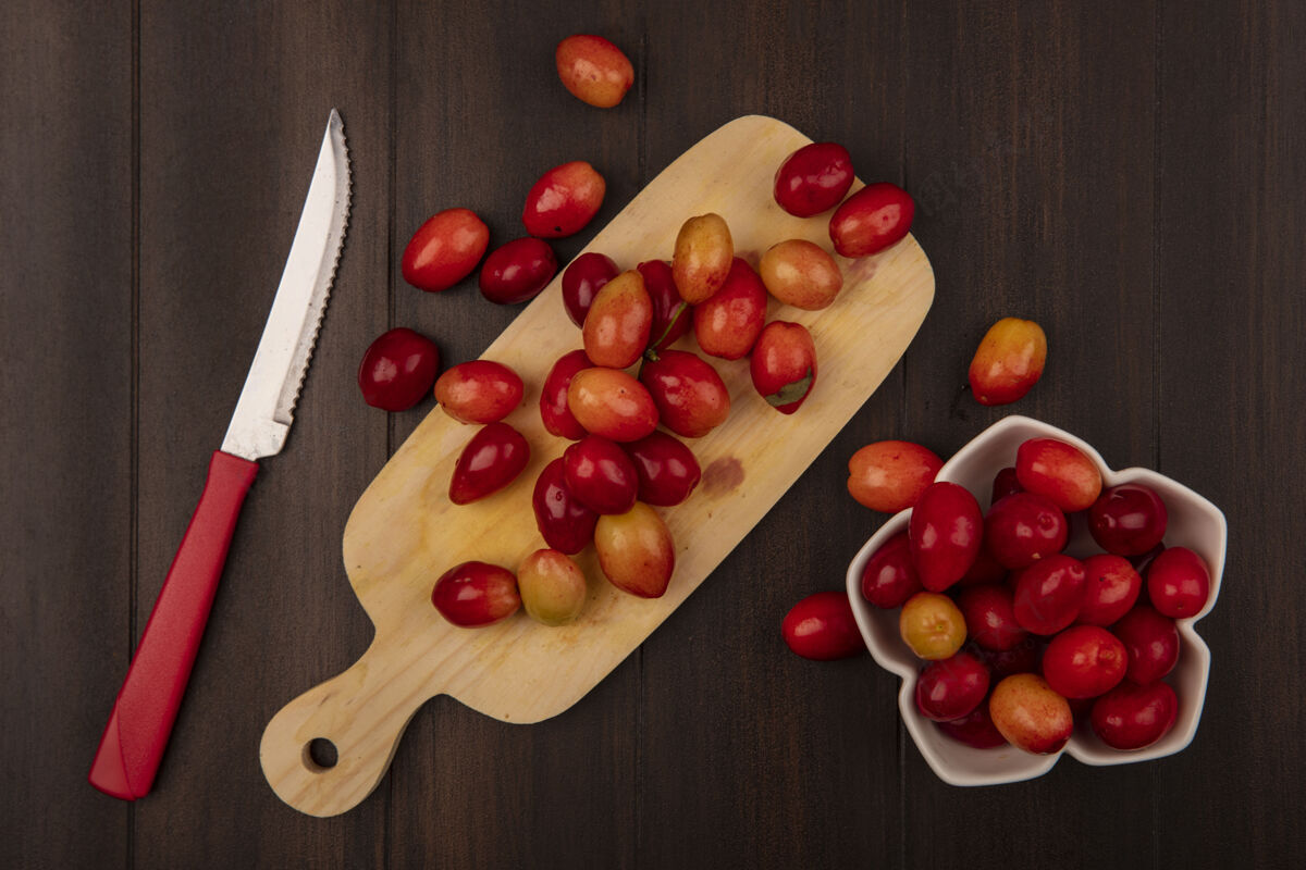刀木制厨房板上的甜甜的酸的山茱萸樱桃的俯视图 木制墙上的碗上有一把刀和山茱萸樱桃视图樱桃顶部
