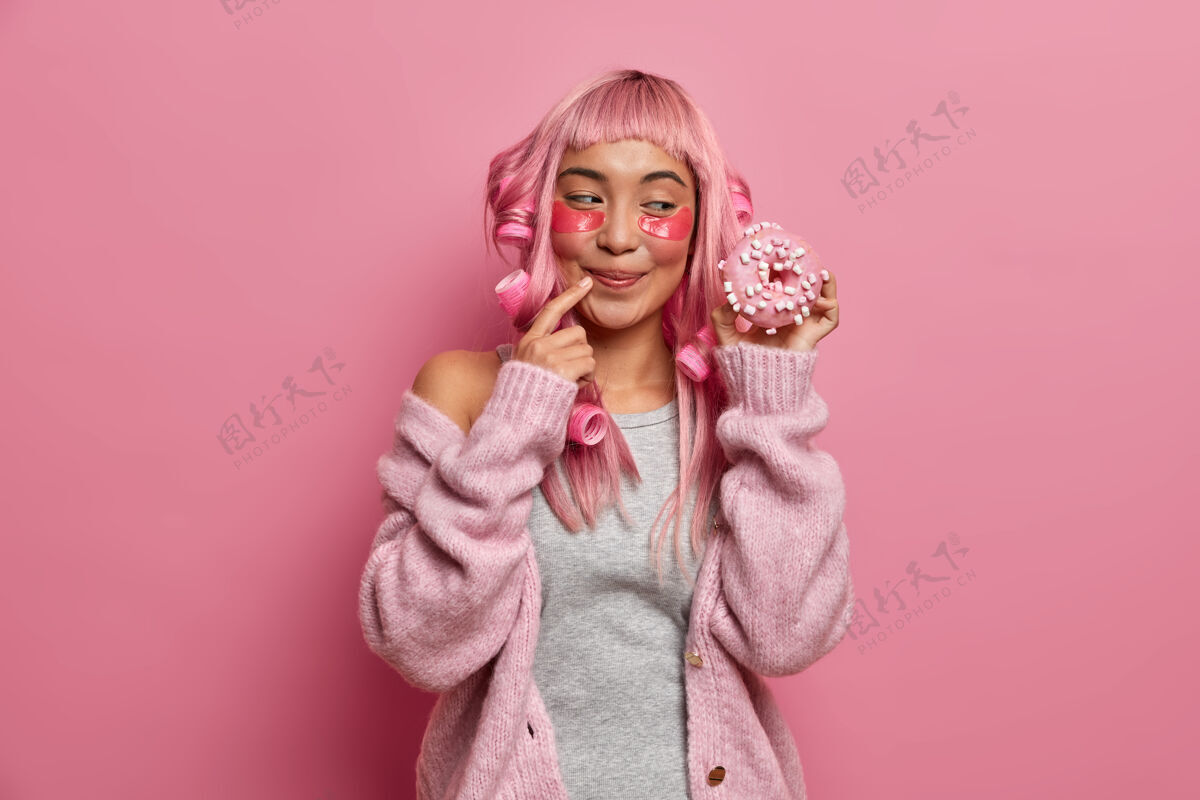 肖像照片中 一个满脸笑容的女人喜欢吃甜食 胃口大开 戴着卷发器 留着粉红色的发型粉色头发应用蓬松