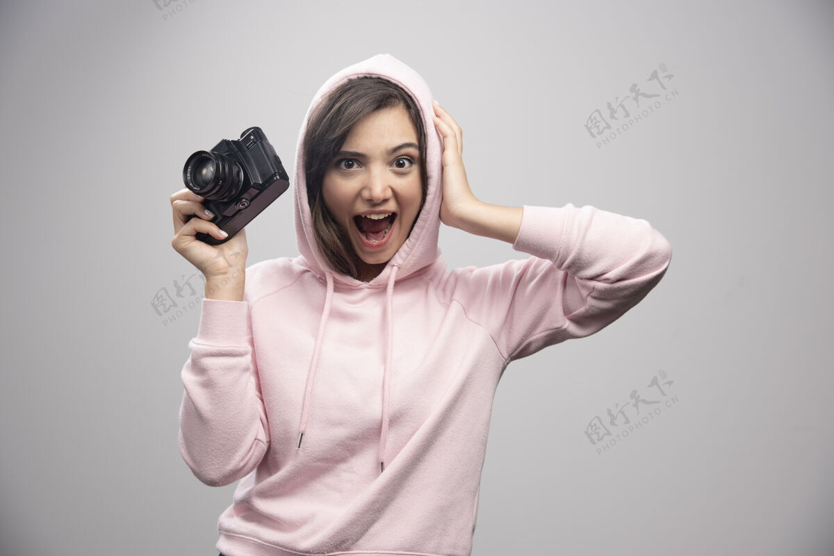 女孩穿着运动衫的年轻女子高高兴兴地拿着相机爱好休闲肖像