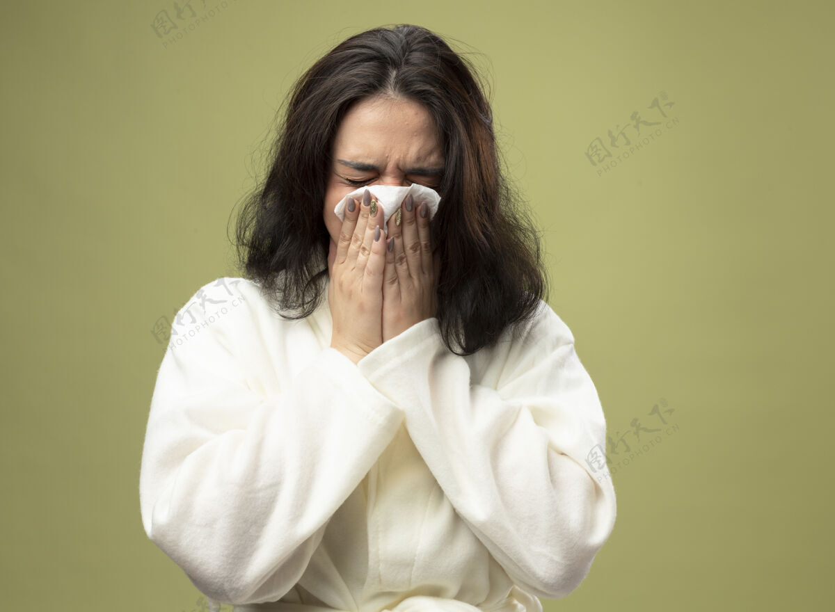 疾病年轻的白种人生病的女孩穿着长袍 用餐巾擦鼻子 闭着眼睛 隔离在橄榄绿的背景上女孩湿巾餐巾