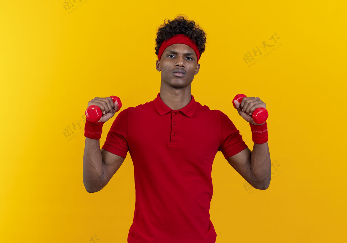 腕带自信的年轻美国黑人运动男子戴着头带和腕带锻炼哑铃隔离在黄色墙上头带非裔美国人哑铃
