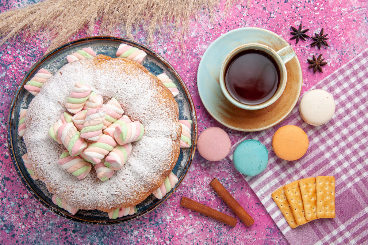 饼干顶视图的糖粉蛋糕与麦卡龙和一杯茶在粉红色的表面茶早餐粉