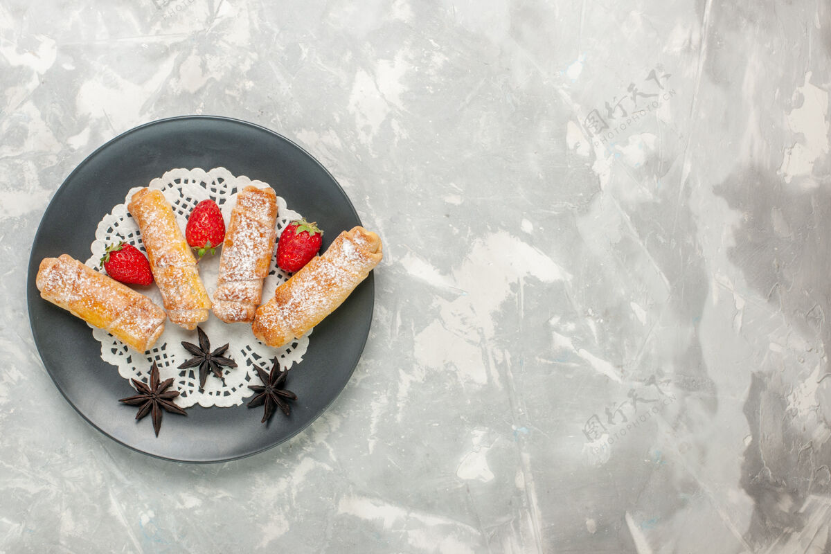 生的糖粉百吉饼的俯视图白色表面上有草莓的美味面团糕点面团糖