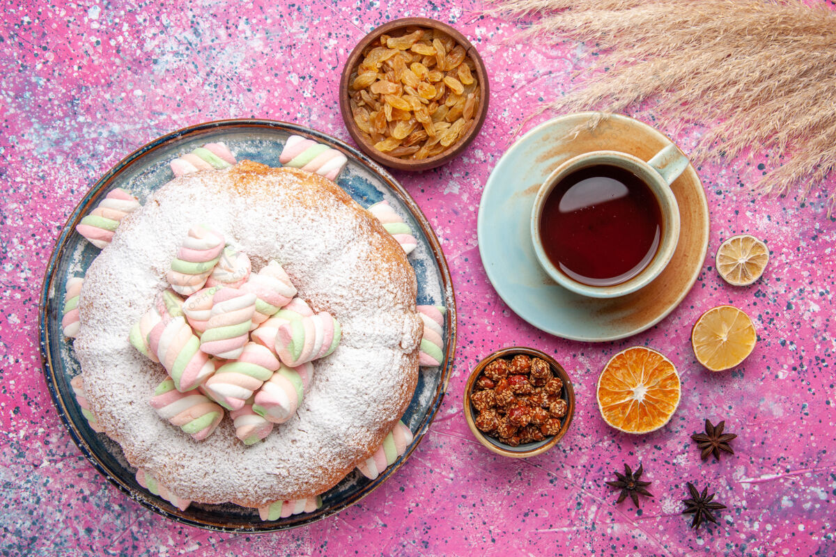 早餐糖粉蛋糕的俯视图 粉色表面上有甜棉花糖和一杯茶饼干含糖食物
