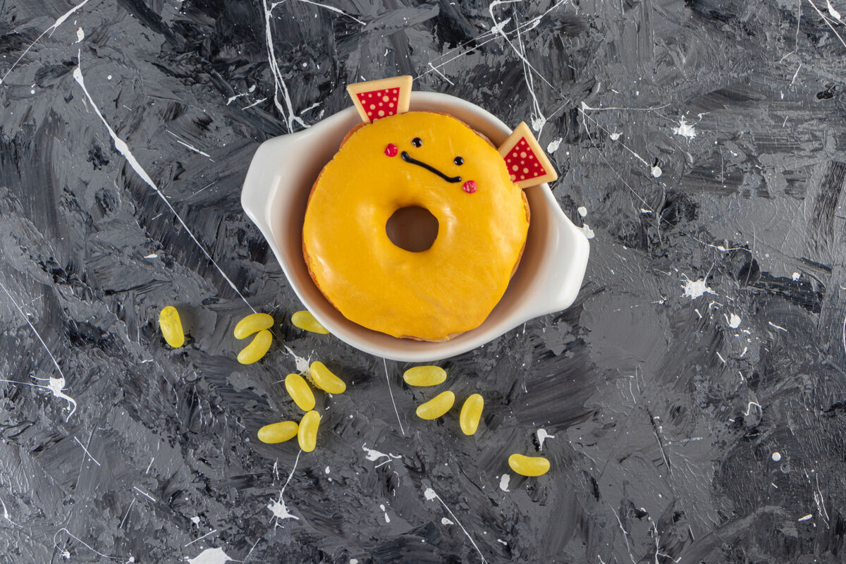 糖果黄色釉面甜甜圈和豆子糖放在大理石桌上烘焙冰食物