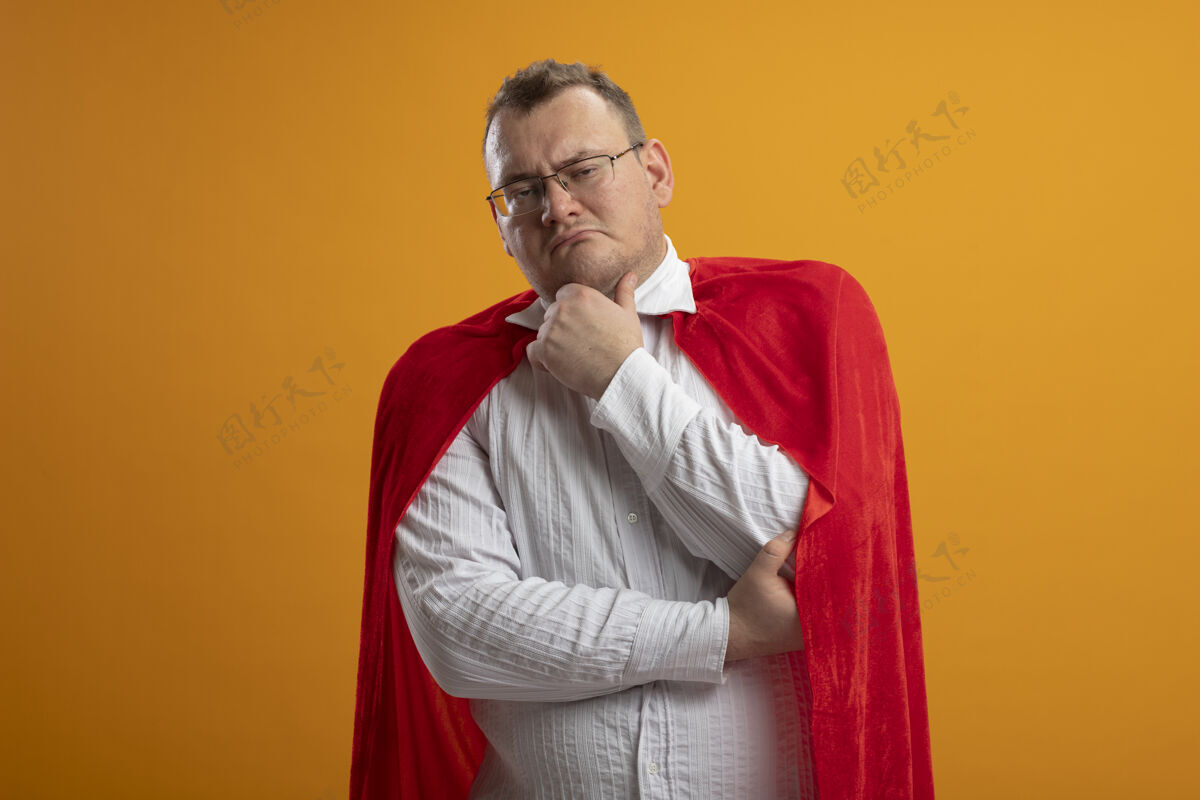 触摸可疑的成年超级英雄 穿着红色斗篷 戴着眼镜 看着被隔离在橙色墙上的下巴穿着人衣服