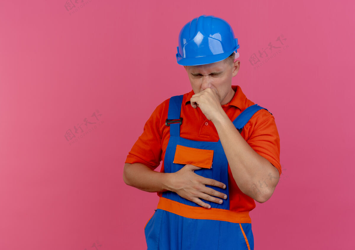 制服年轻的男建筑工人闭着眼睛 穿着制服 戴着粉红色的安全帽头盔男性安全
