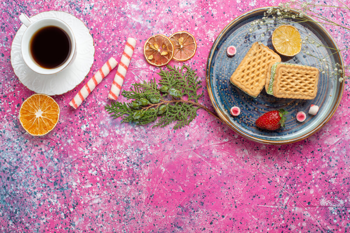 饼干浅粉色表面上的甜华夫饼和一杯茶的俯视图顶视图茶胡椒