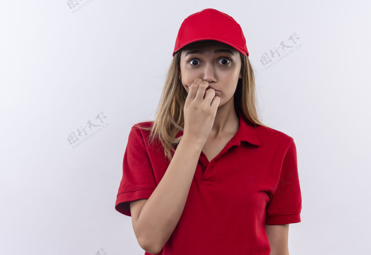 帽子穿着红色制服 戴着帽子 手放在嘴上 隔离在白墙上的关心的年轻送货女孩送货穿着年轻
