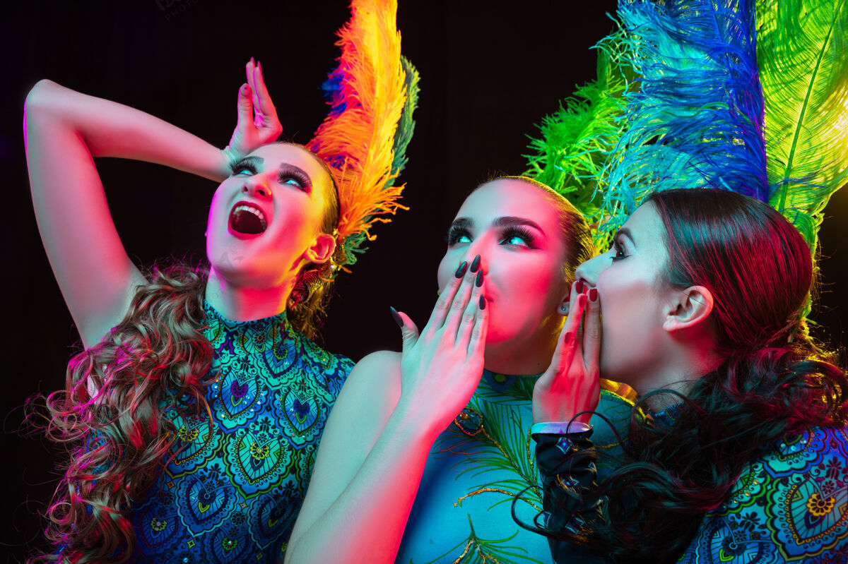 嘉年华特写镜头美丽的年轻女子在狂欢节 时尚的化装舞会服装与羽毛在霓虹灯黑色背景模特庆典女性