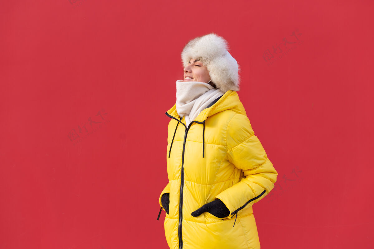 女孩在一个冬天阳光明媚的日子里 穿着暖和衣服的红墙背景上的快乐年轻女子正面完美享受