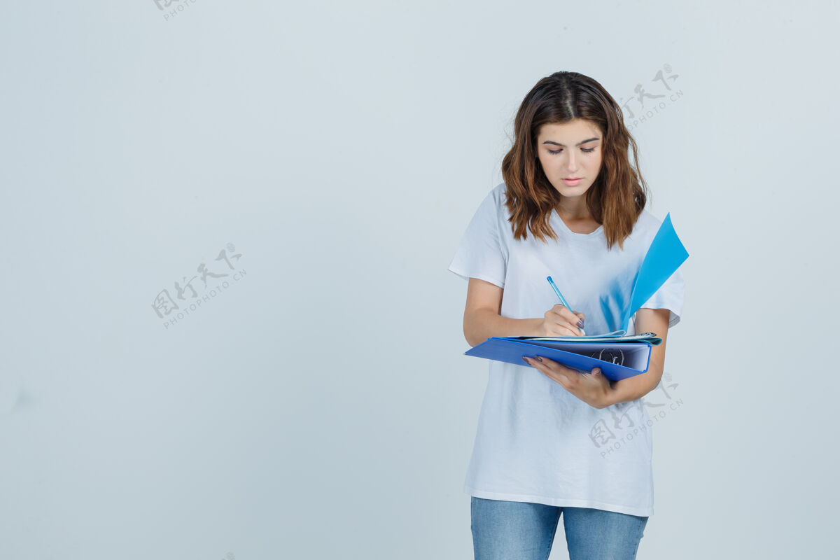 时尚年轻女性穿着白色t恤 牛仔裤在文件夹上做笔记 看上去很忙 正对着前方看女性人前面
