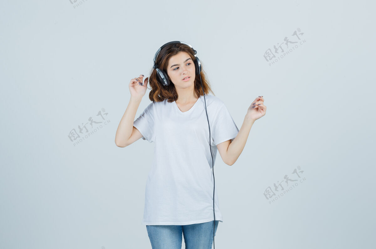 快乐穿着白色t恤 牛仔裤 戴着耳机欣赏音乐的年轻女性的肖像 看起来像梦幻般的前景色前面护理乐趣