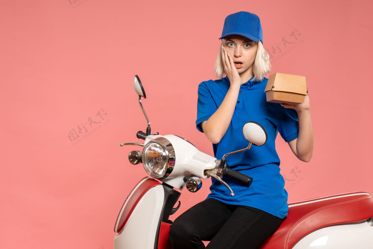 工作前视图骑着自行车的女快递员 粉红色的小食品包摩托车自行车服务