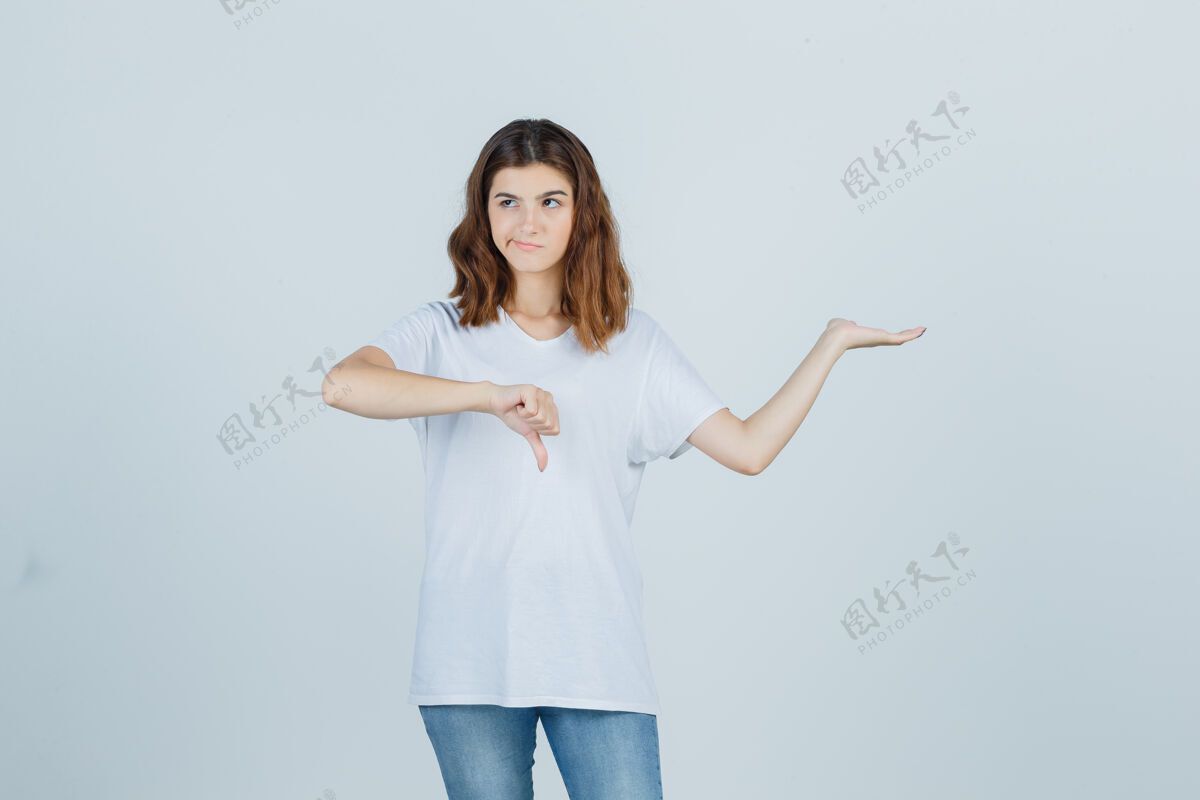隔离穿着白色t恤的年轻女孩展示着拇指朝下的欢迎手势 看上去犹豫不决年轻街道向下