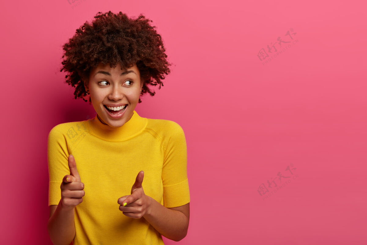 非洲积极的黑皮肤年轻女性点 选择你 感到快乐和放松 高兴地咯咯笑 看一边 穿黄色t恤 对着粉色墙壁摆姿势 复制空间一边女人咯咯笑年轻