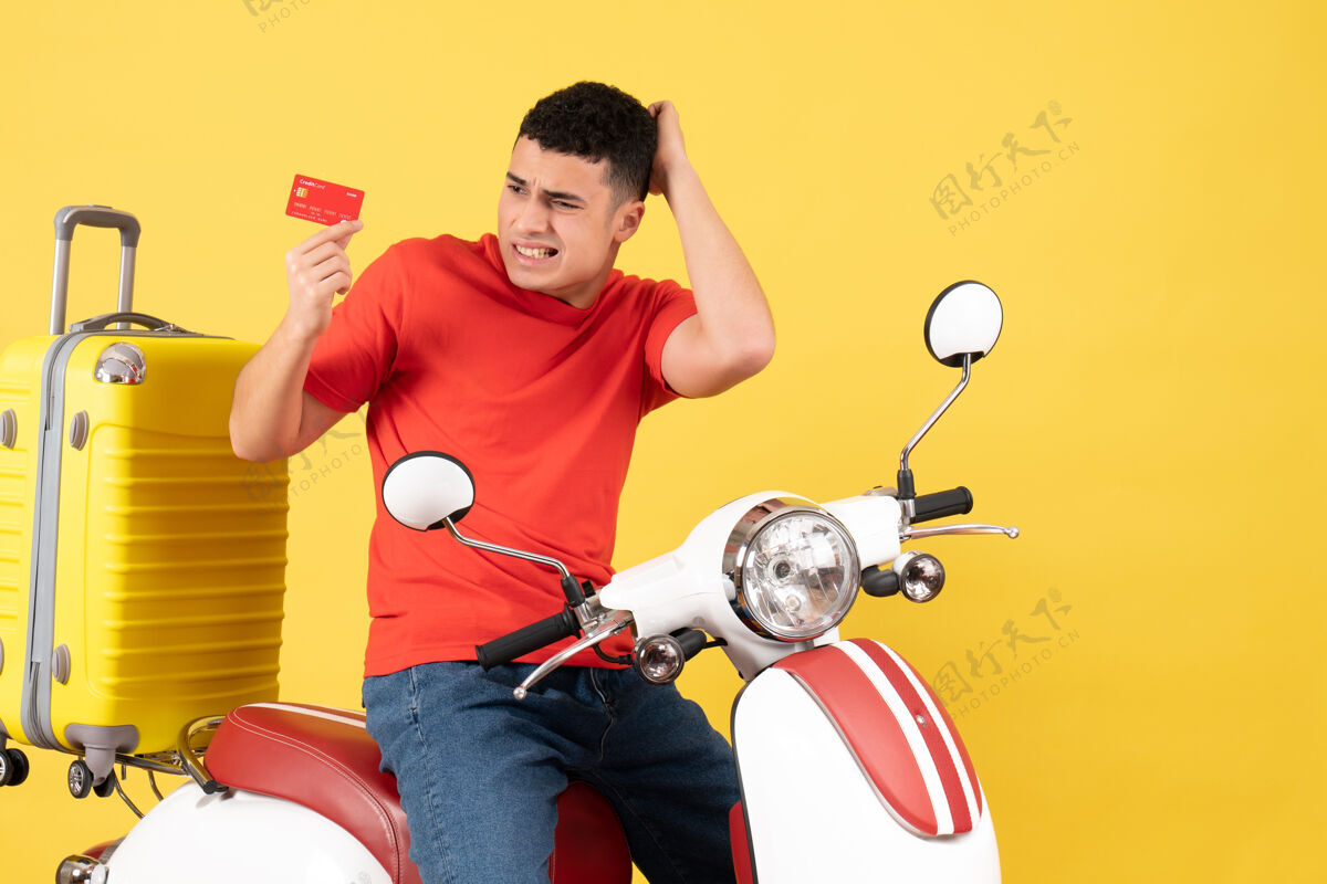 活跃前视图困惑的年轻人穿着红色t恤在轻便摩托车持卡T恤轻便摩托车微笑