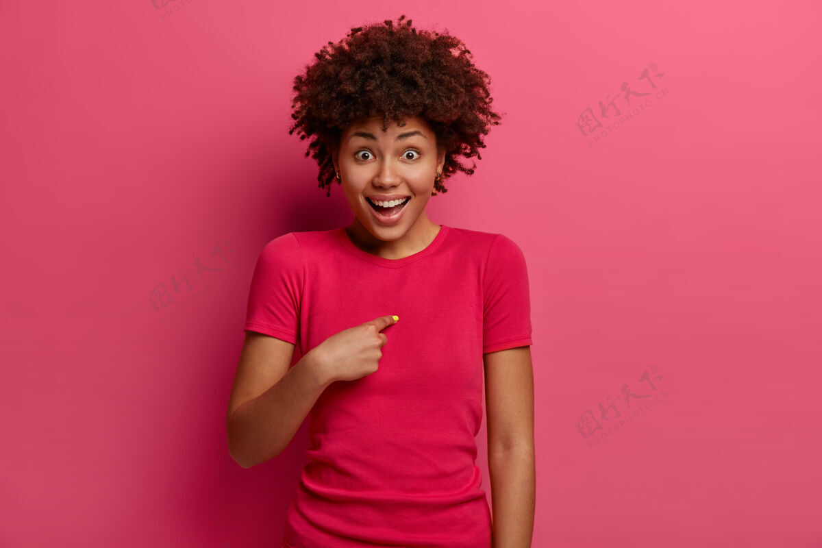 种族积极的非洲裔美国年轻女子兴奋地指着自己 有高兴的意外反应 问你在开玩笑吗 积极地笑 穿着红色t恤 对着粉色的墙摆姿势青少年年轻脸