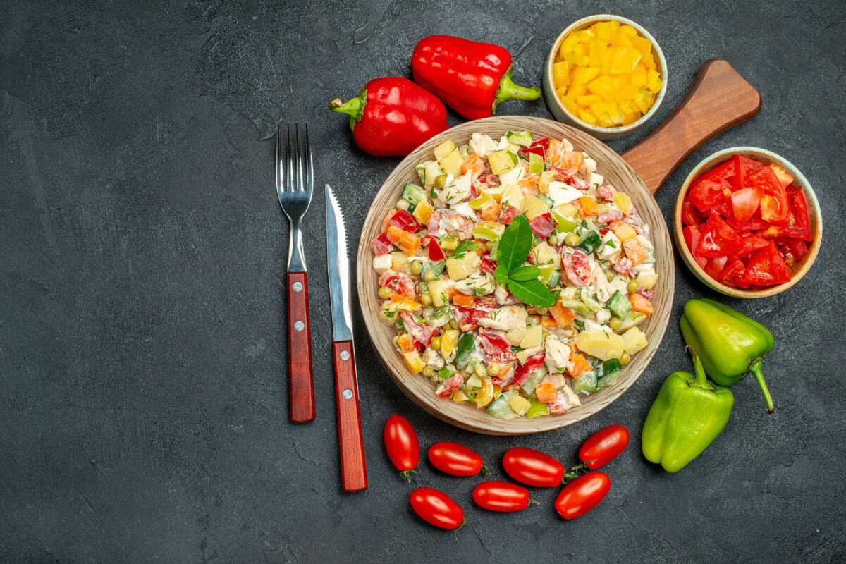 午餐蔬菜沙拉的顶视图 旁边有餐具和蔬菜 在深灰色的背景上可以自由放置文本文字深色背景