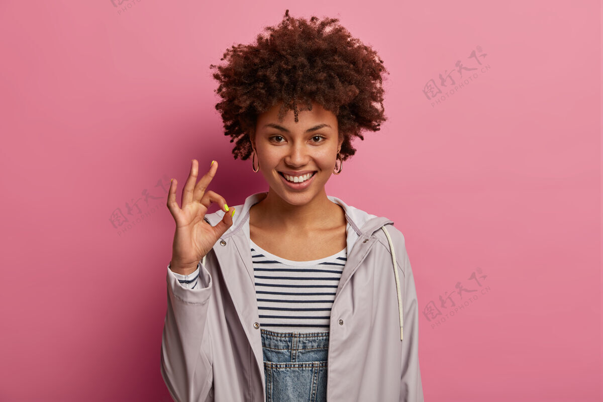 欢呼微笑积极的非洲裔美国妇女同意你的意见 给予推荐并留下良好的反馈 有愉快的表情 提出建议 穿灰色的休闲服 在玫瑰色的墙上摆姿势高兴好印象
