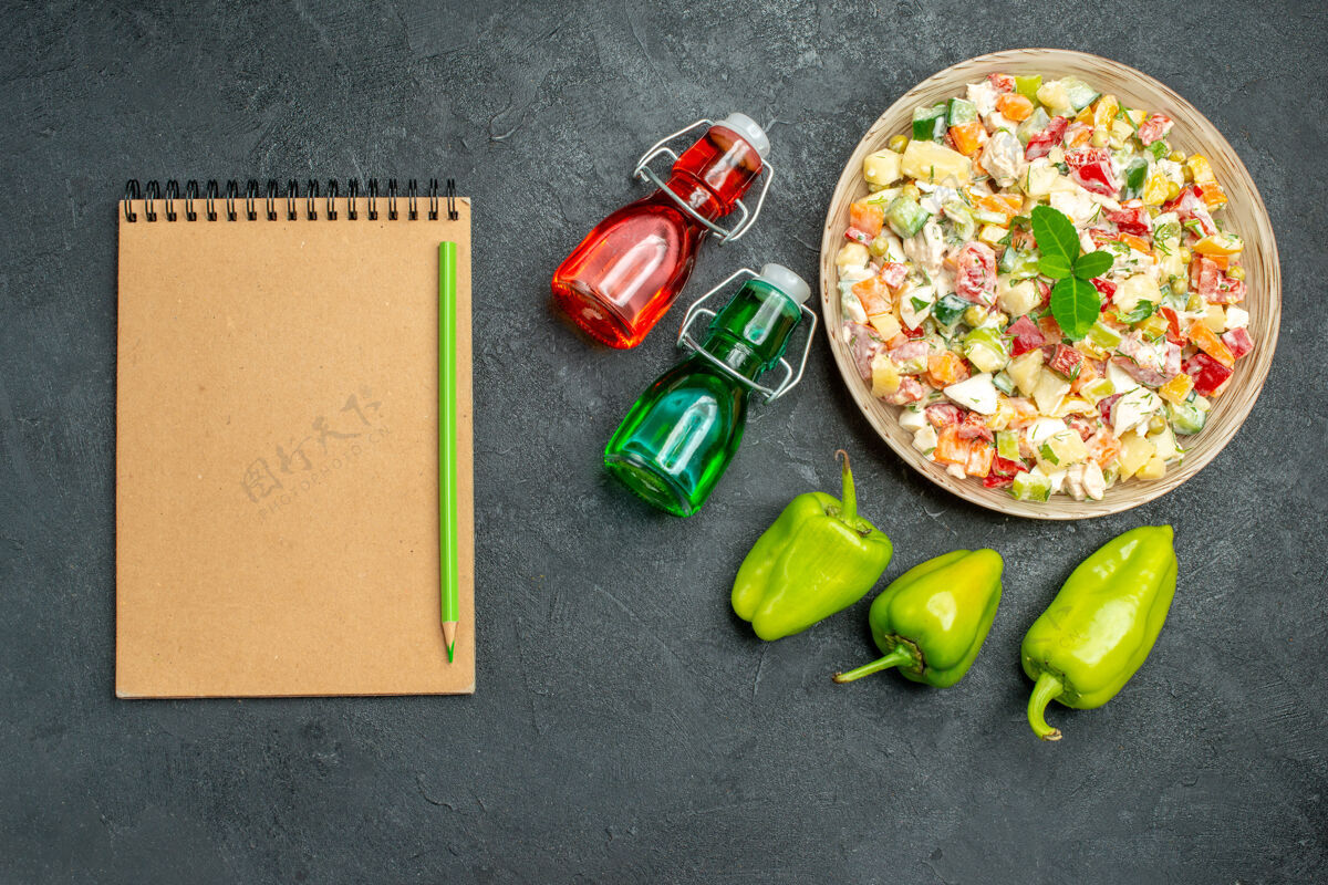 胡椒一碗蔬菜沙拉的顶视图 深绿色桌子上有甜椒记事本和油醋瓶瓶子水果铃铛
