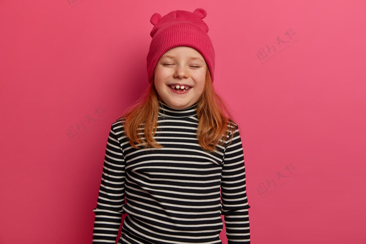 条纹孤立镜头中的红发女孩积极地笑着 戴着粉色的帽子和条纹的套头衫 非常情绪化 来参加生日聚会 孤立在粉色的墙上快乐的情绪概念红发乐观肖像