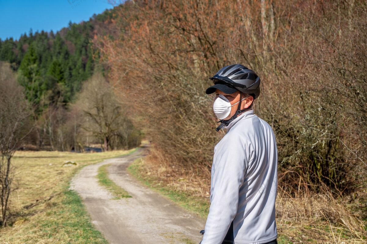 娱乐戴着防护面具的人在冠状病毒\/冠状病毒-19期间骑自行车自然道路单独
