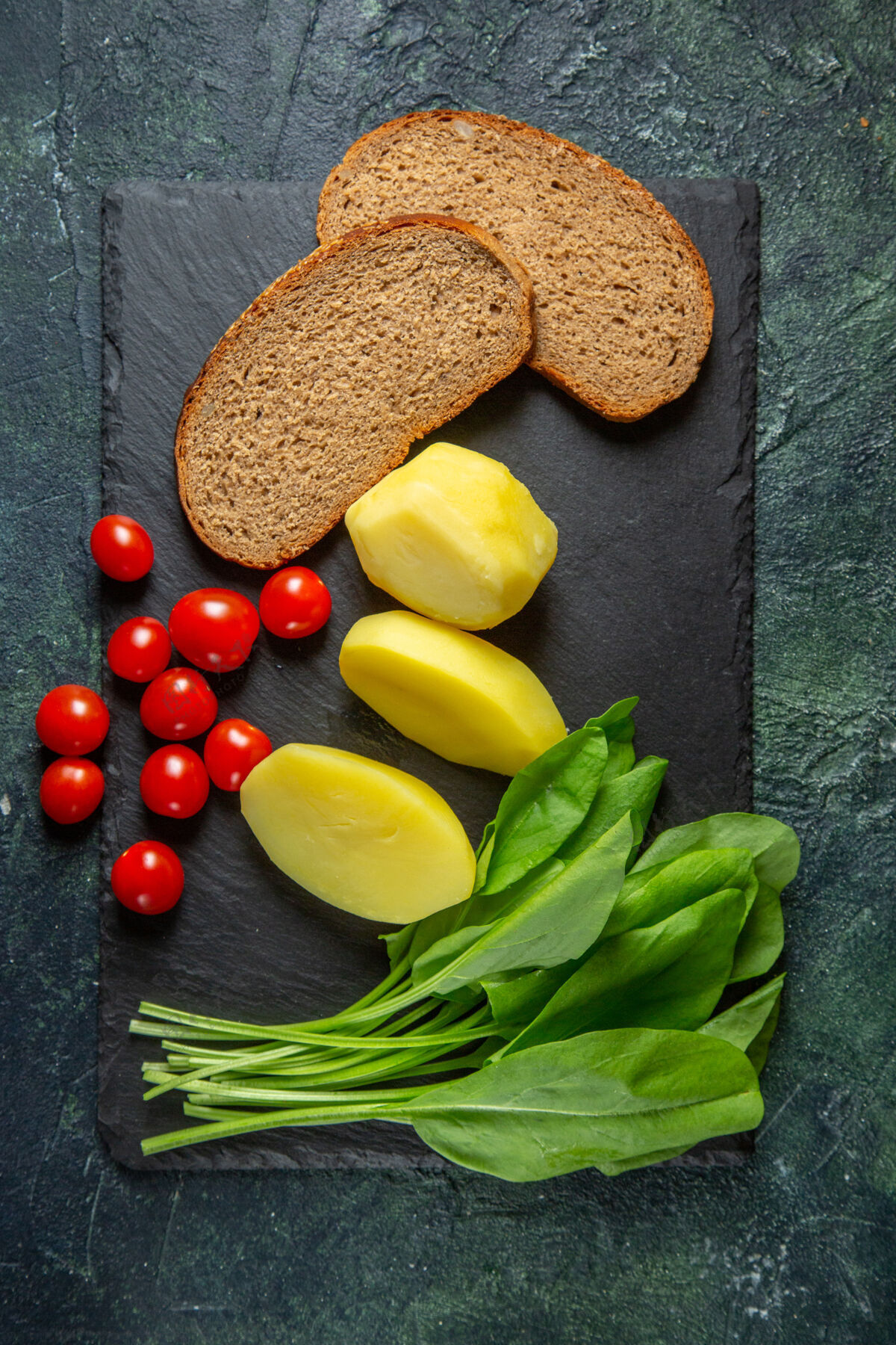 蔬菜新鲜去皮切土豆和膳食面包片的垂直视图西红柿绿色捆绑在木质砧板上绿色黑色混合色背景饮食切片垂直