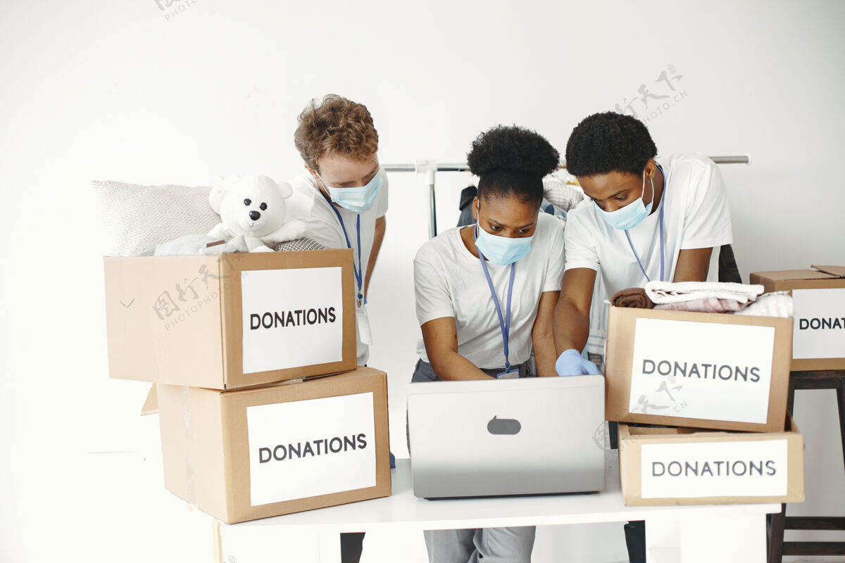 慈善带着复选框的男男女女戴着面具的志愿者带着笔记本电脑盒子带着人道主义援助防护流行病团队