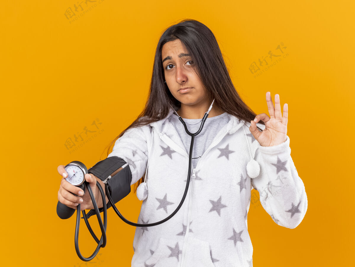 年轻悲伤的年轻生病的女孩用血压计测量自己的血压 显示出良好的姿势 隔离在黄色背景上悲伤好疾病