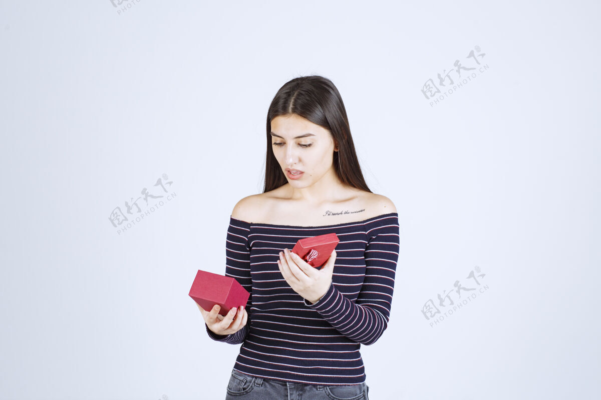 工人穿条纹衬衫的女孩打开一个红色的礼盒 感到困惑失望人体模特摆姿势