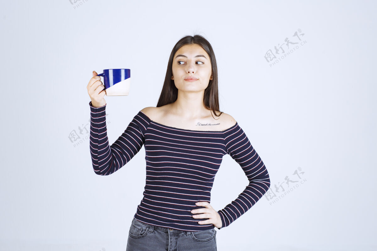 女人穿条纹衬衫的女孩看着咖啡杯 感到不满意品味随意年轻