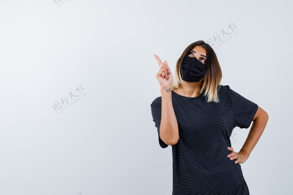 前面身穿黑色连衣裙的女士 医用面罩指着左上角 面带沉思 正视图现代头发夏天