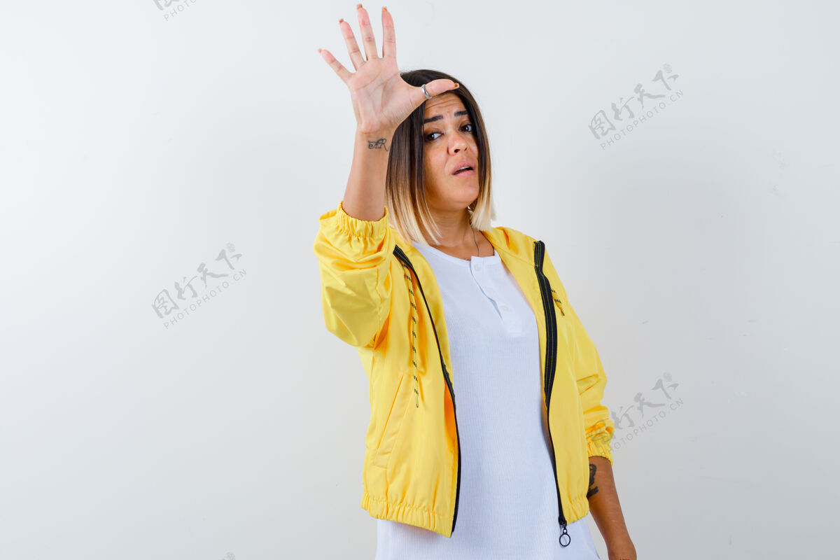 面部身穿白色t恤 黄色夹克的年轻女孩展示停车标志 看上去很自信 正面视图自信前面金发