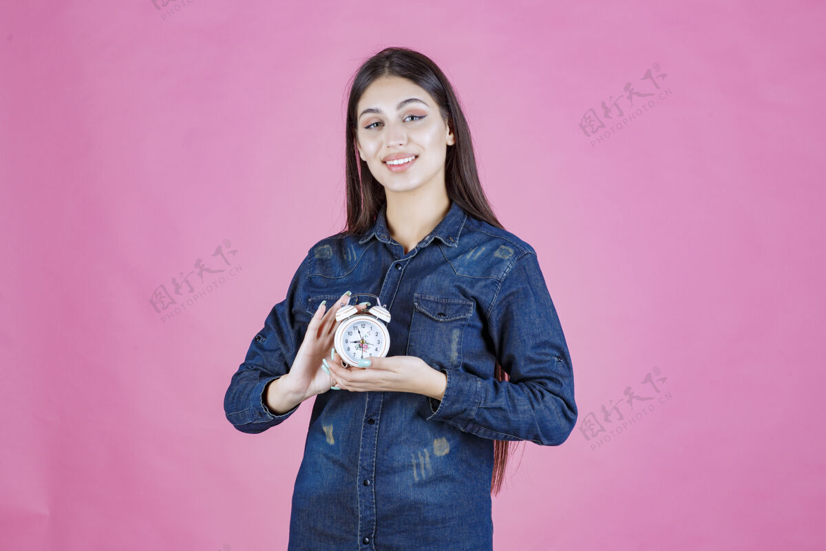 女性穿着牛仔衬衫的年轻女子双手抱着闹钟销售人年轻