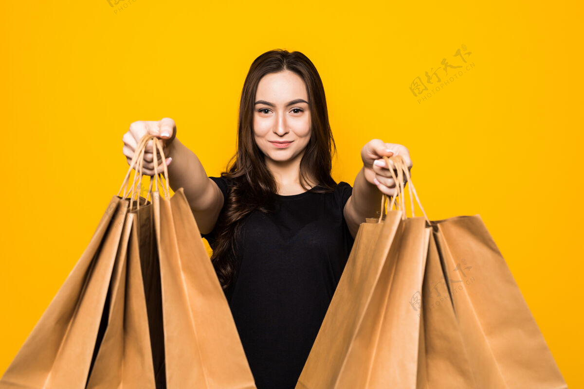 人快乐的年轻女子拿着购物袋站在黄色的墙上购买持有时尚