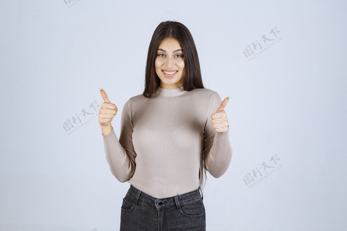 积极穿灰色毛衣的女孩在做竖起大拇指的招牌员工姿势享受