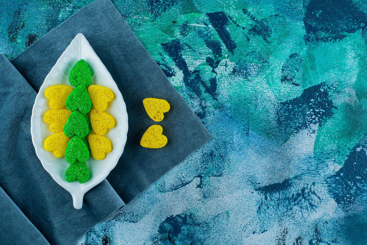 糕点黄色和绿色的甜饼放在一块布上的盘子上 背景是蓝色的糖五颜六色饼干