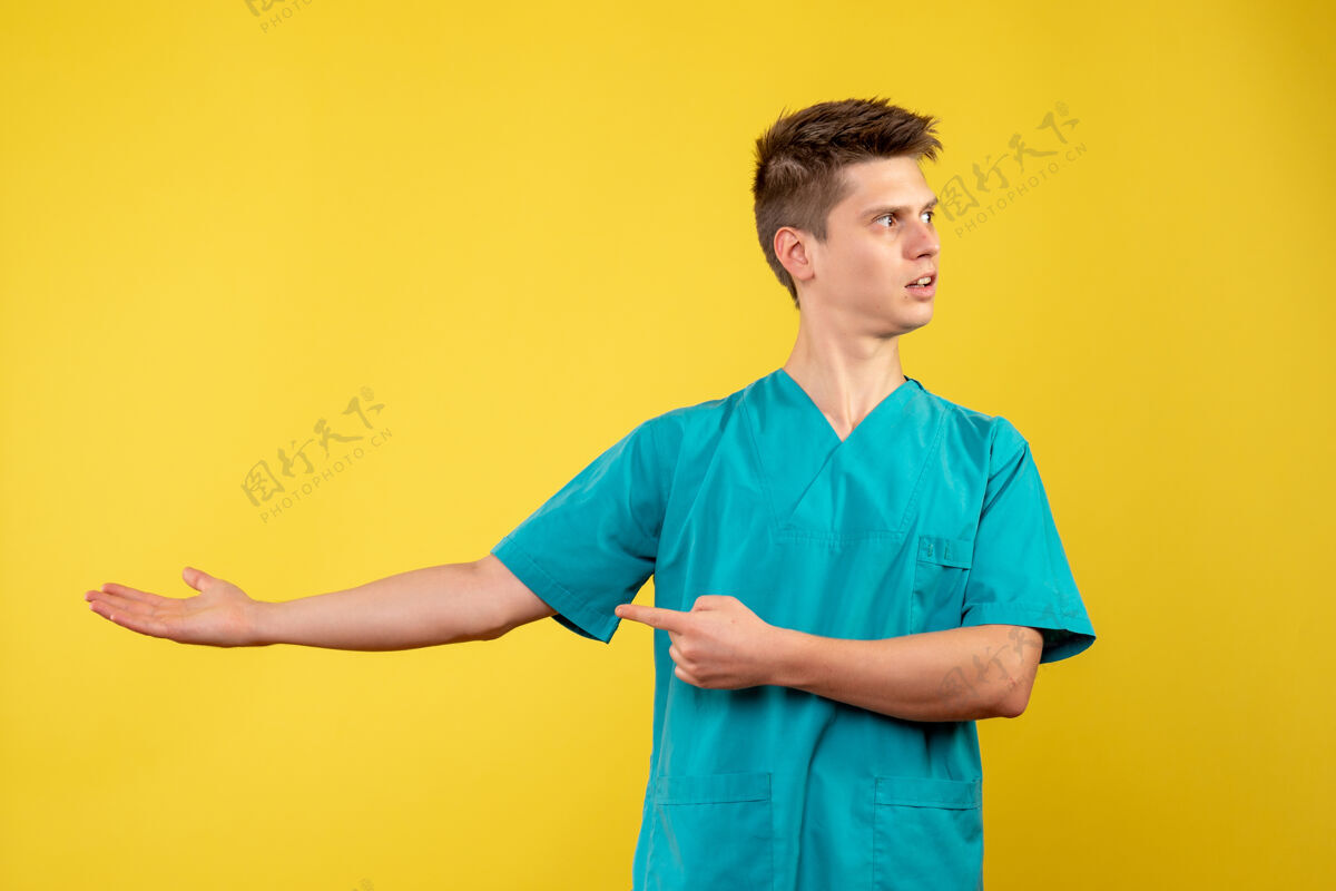 自信黄色墙壁上穿着医疗服的男医生的正视图男性健康微笑