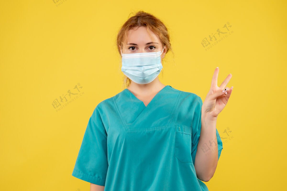 正面黄色墙壁上戴着无菌防护面具的女医生的正视图防护医疗医生