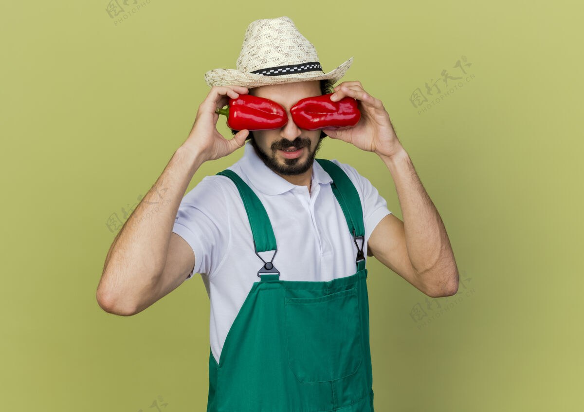 橄榄戴着园艺帽的戴眼镜的年轻男园丁用红辣椒闭上眼睛胡椒园艺男性