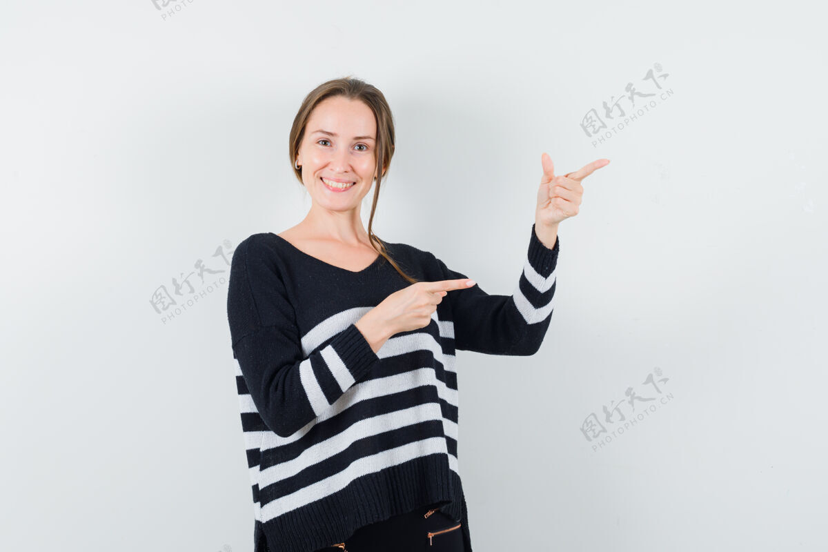 脸穿着条纹针织衫和黑色裤子的年轻女子用食指指着右边 看上去很开心肖像护理健康