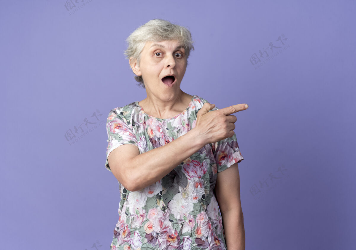 老惊讶的老妇人指了指紫色墙上看起来孤立的一边紫色老老