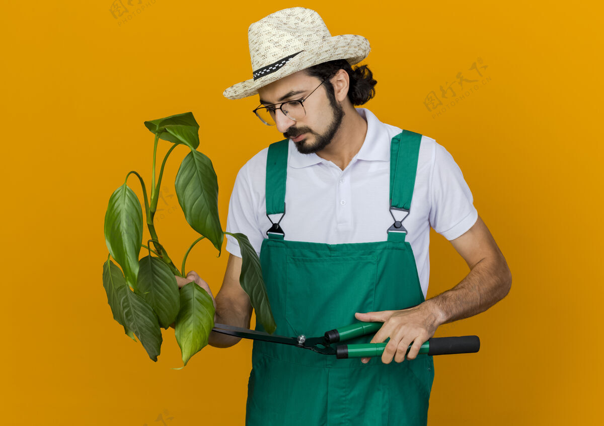 园艺自信的男园丁戴着眼镜 戴着园艺帽 拿着剪刀 看着植物眼镜复制橙色