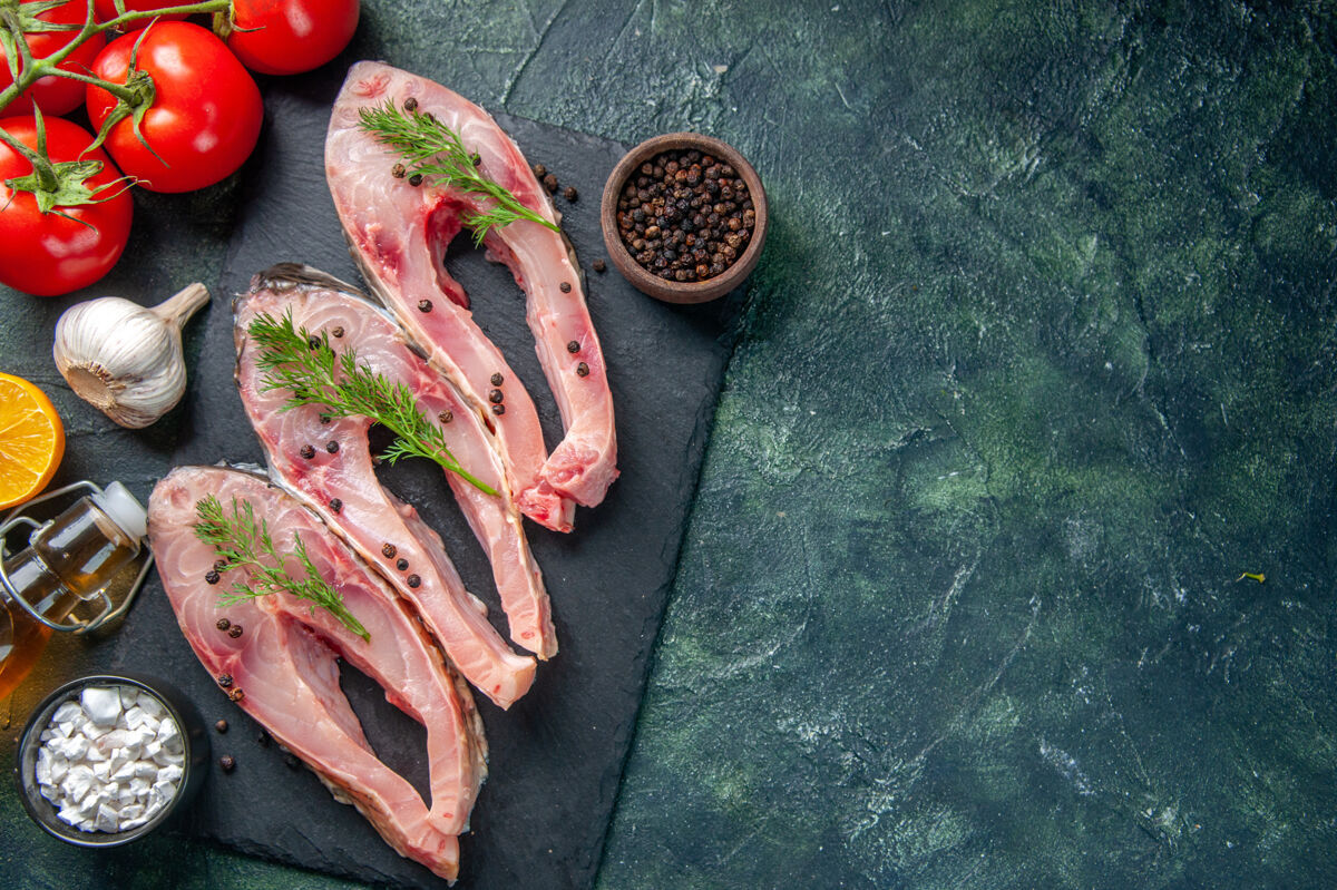 盘子顶视图新鲜鱼片 深蓝色背景上有胡椒和西红柿胡椒晚餐深色